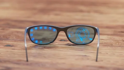 Pair of blue smart glasses laying on a wooden desk. AR overlay showing functions Video stock 202276640
