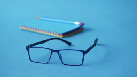 Pair of blue spectacles with stack of colorful notebooks and pencils on lig.. Vídeos de archivo 333151984