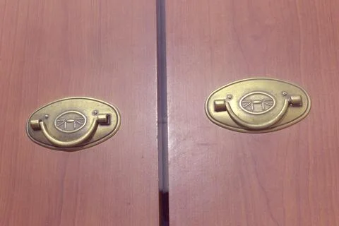 Pair of brass folding pull handles on the wooden doors of wardrobe Stock Photos