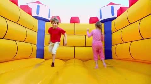 Pair of children boy and girl jump at inflatable playground Stock Footage