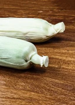 Pair of ears of corn whole vegetables with green leaves on wooden tinted back Stock Photos