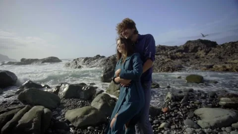 The pair embrace against the backdrop of black rocks and splashes of waves. The Stock Footage 219334328