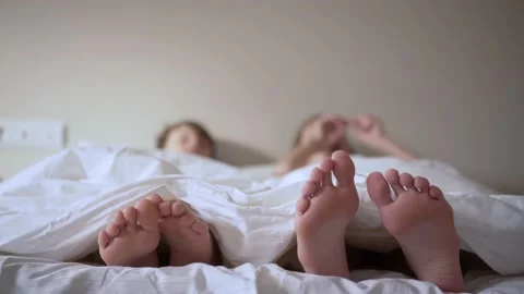 Pair of feet in bed on white sheets. Child lies in bed in the morning and moves Stock Footage 158877385