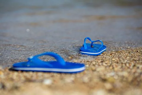 Pair of flip flops on the beach and water flow. Stock Photos