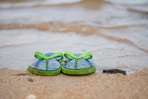 A pair of green slippers in a seaside with sands in a tranquil exotic weather Stock Photos