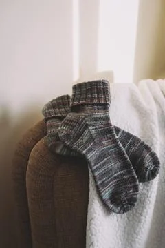 Pair of hand knitted socks on the sofa in a sunlight. Natural colors. Stock Photos