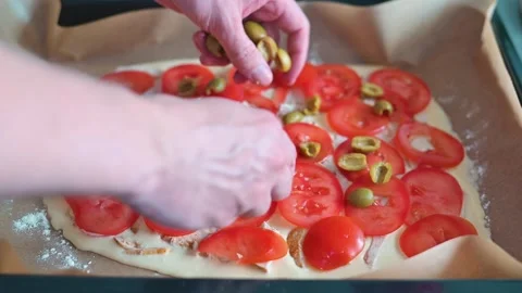 A pair of hands adds sliced tomatoes and olives to a flat surface in a kitchen. 動画素材 339096370