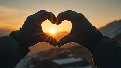 Pair of hands in gloves forms heart shape against sunset in mountains Stock Footage 300677720