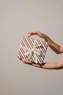 A pair of hands holding a single Christmas present with festive striped paper Stock Photos