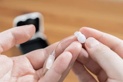 A pair of hands holds a modern digital hearing aid device, highlighting careful Stock Photos