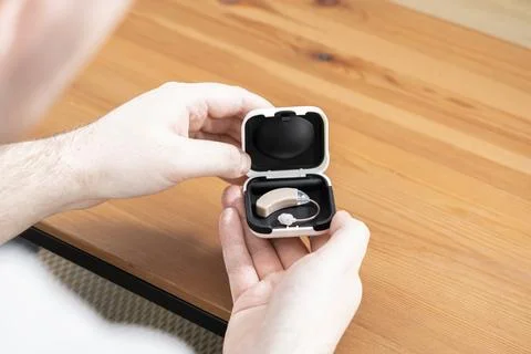 A pair of hands holds an open case with a beige hearing aid inside, Stock Photos