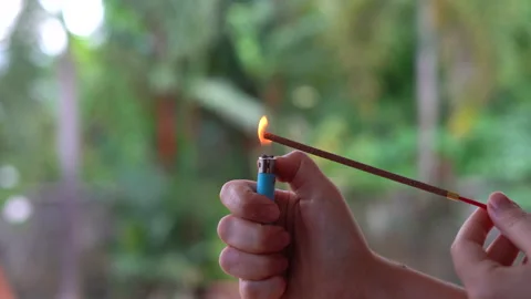 Pair of hands lighting incense using a lighter against the backdrop of trees Stock Footage 236700569