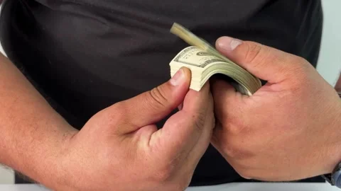 A pair of hands meticulously counts a wad of cash, reflecting the stress of Stock Footage 295656234
