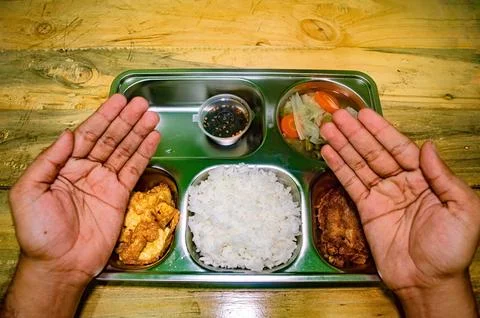A pair of hands shown in a prayer-like gesture over a metal tray containing.. Stock Photos