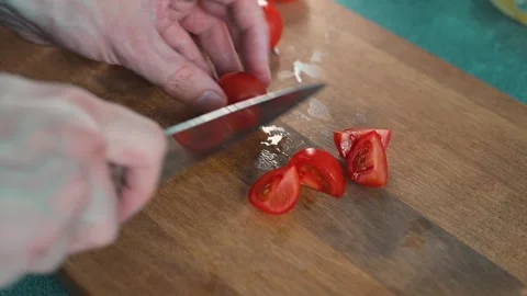 A pair of hands skillfully chop cherry tomatoes on a wooden cutting board in a 库存影片 338290633