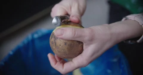 Pair of hands skillfully peeling potato while hovering above trash bin Stock Footage 299903429