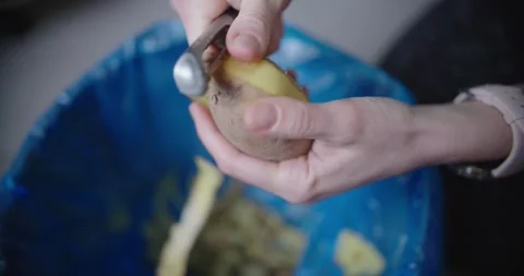 Pair of hands skillfully peeling potato while hovering above trash bin Stock Footage 299903459