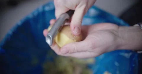 Pair of hands skillfully peeling potato while hovering above trash bin Video stock 299903492