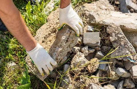 Pair of hands wearing white gloves holding a large piece of broken concrete.  Stock Photos
