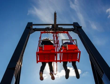 Pair having fun in swing on a high building against blue sky Stock Photos