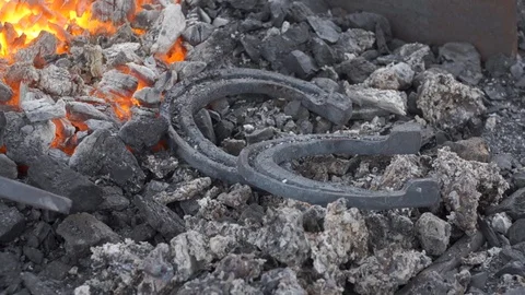 A pair of horseshoes cools in a forging brazier. Stock Footage 120572635