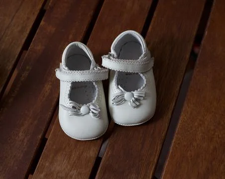 Pair of infant baby shoes with bowknot on wooden background. Stylish baby sho Stock Photos