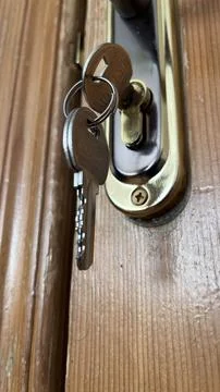 A pair of keys is inserted in a lock on a wooden door. The view focuses on th Stock Photos