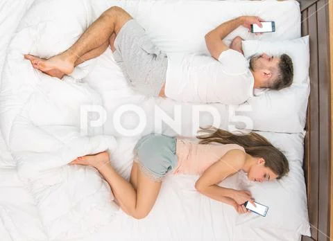 The pair lay on the bed and phone. View from above Stock Photos