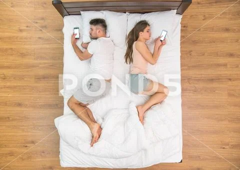 The pair lay on the bed and phone. View from above Stock Photos