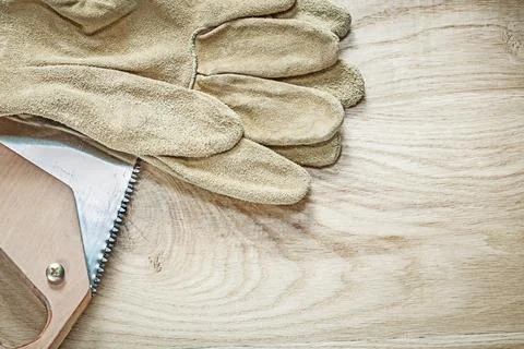 Pair of leather safety gloves Sharp hacksaw on wooden board Construction concept Fotos Stock