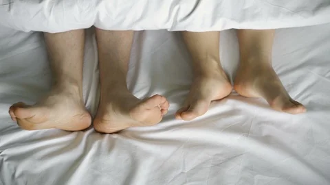 A pair of legs dancing under a white blanket, on a white bed, top view.4k Stock Footage 106290478