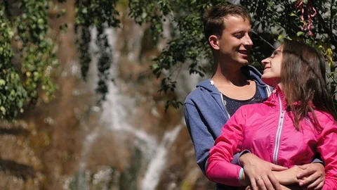 A pair of lovers stand against a waterfall. Honeymoon. kiss on the background of Vidéo 106102122