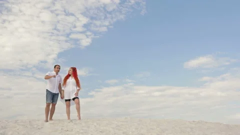 Pair of lovers stands on the white sand against the blue sky in white clouds Stock Footage 137383290
