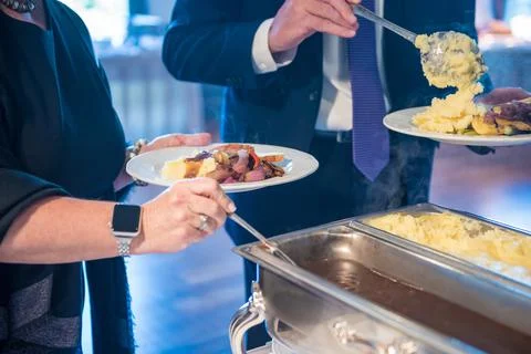Pair of men serving themselves with mashed potatoes and meat at a public even Fotos Stock