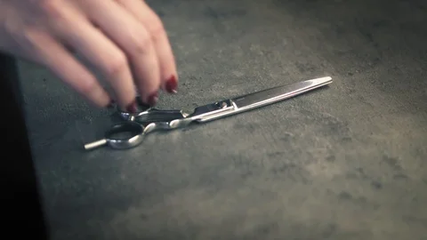 A pair of metal scissors lies on the table and a female's hand with lovely red Stock Footage 86713751