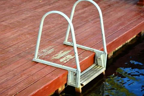 A pair of metal steps situated at the end of a wooden dock, perfect for getting Stock Photos