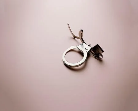 Pair of metallic handcuffs over a flat and bright pastel pink background Fotos Stock