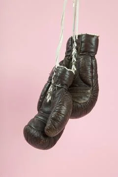A pair of old boxing gloves hung in front of a candy-pink background Stock Photos