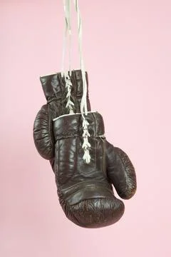 A pair of old boxing gloves hung in front of a candy-pink background Stock Photos
