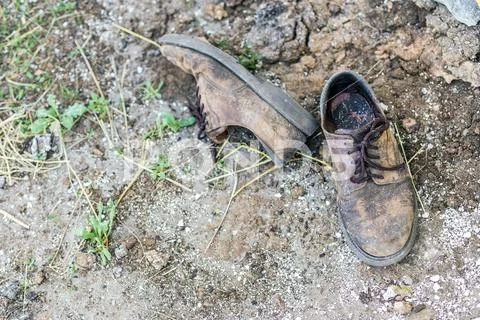 Pair of old dirty used shoes. Abandoned discarded boots laying in dust on groun Stock Photos