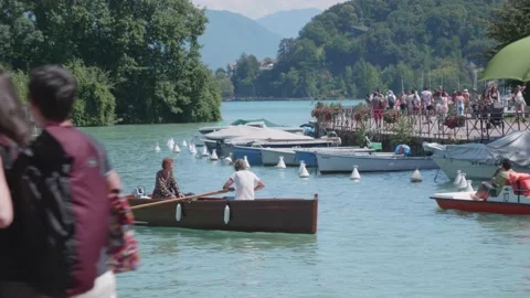 Pair of people floating on row boat while tourists walking on waterfront Stock Footage 157007516
