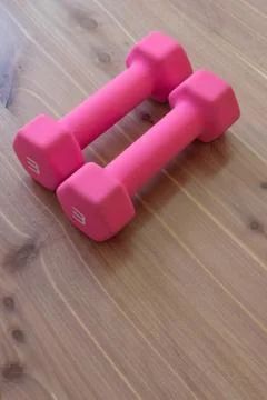 Pair of pink hand weights side by side on a light neutral wood background Stock Photos