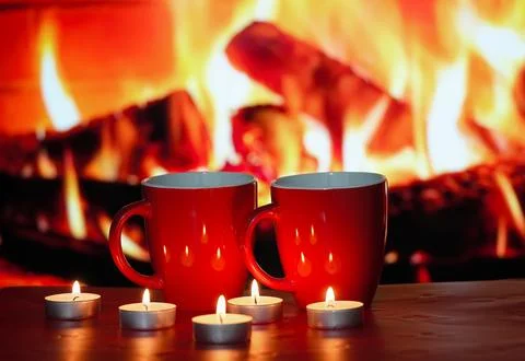 A pair of red cups and burning candles against the fire fireplace. Stock Photos