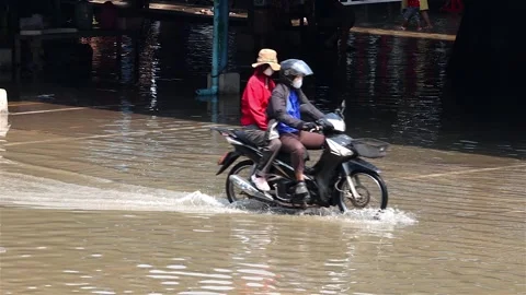 A pair rides a bicycle through a flooded street,Thailand Stock Footage 269285419