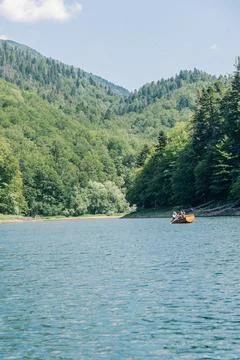 Pair rowing small boat across forest Biogradsko lake with oar in water and .. Photos