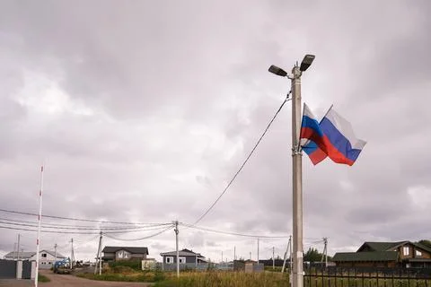 Pair of Russian flags flying from light pole in a village under cloudy sky. Stock Photos