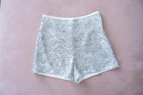 A pair of sequined silver shorts displayed on a soft pink surface. Stock Photos