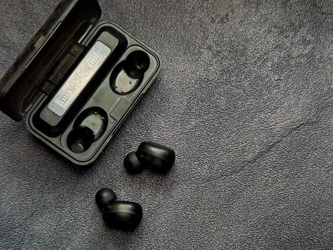 A pair of sleek black wireless earbuds are displayed next to their open cha.. Stock Photos