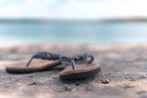 Pair of slippers on the sand at the beach while a blurry background. Stock Photos