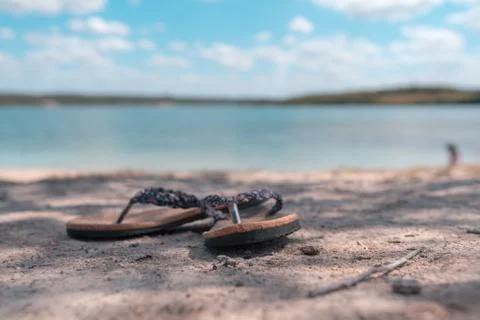 Pair of slippers on the sand at the beach while a blurry background. Stock Photos